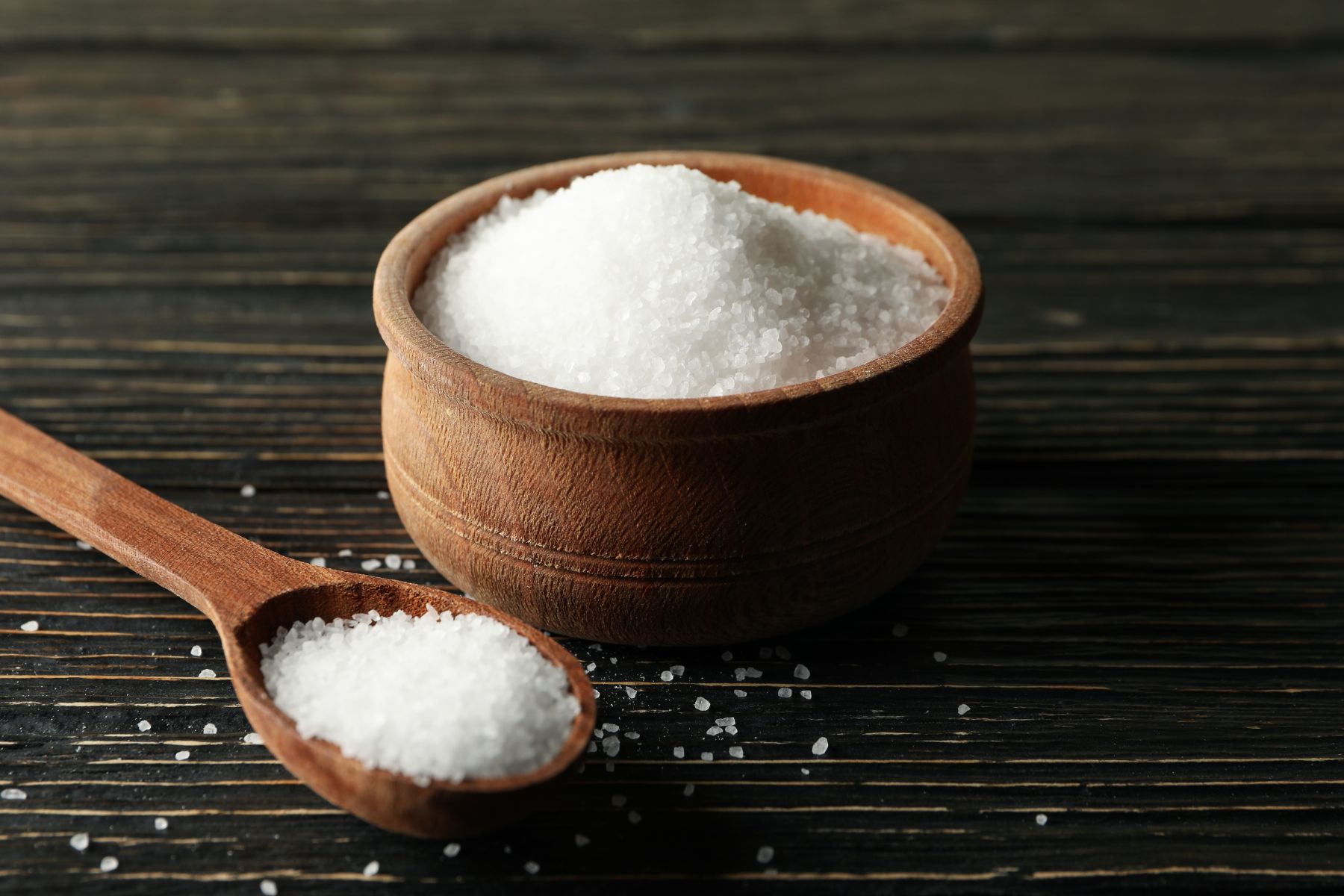 Spoon and bowl with salt on wooden background