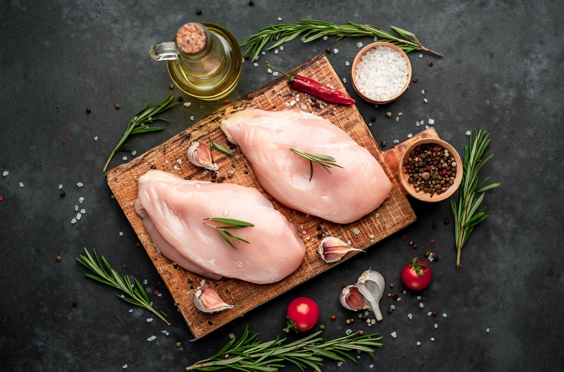 
Raw chicken fillet on a cutting board with rosemary, spices, tomatoes and pepper on a stone background; Shutterstock ID 1582498705; purchase_order: KFT; job: Europe; client: Marketing