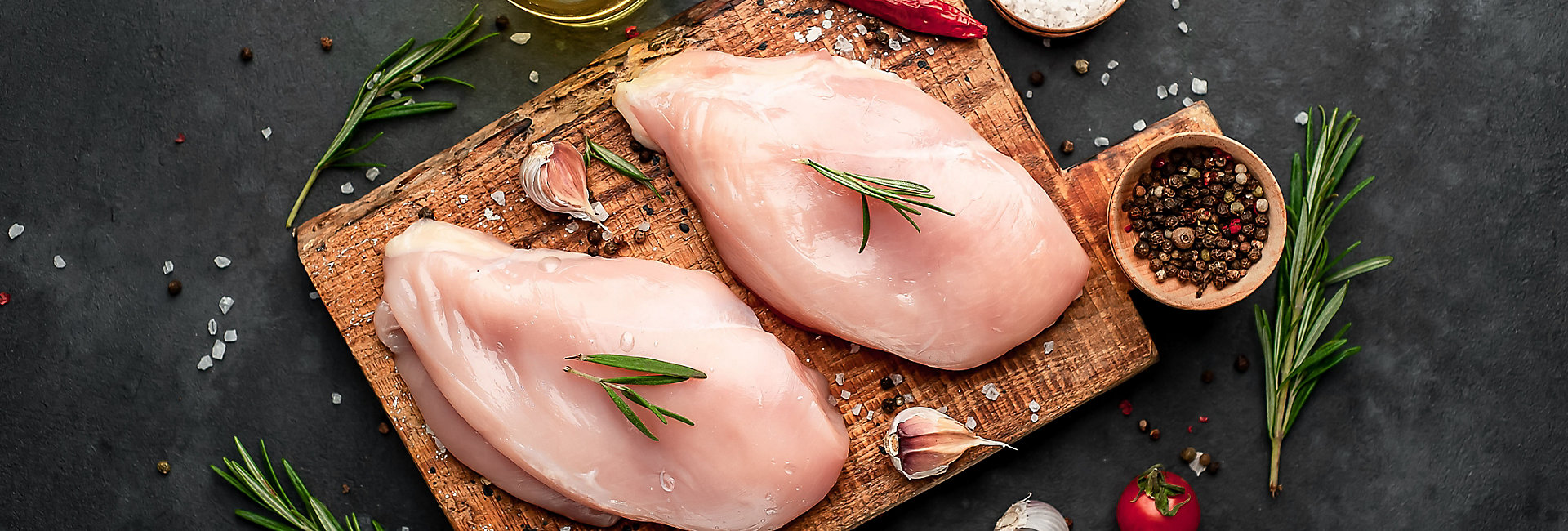 
Raw chicken fillet on a cutting board with rosemary, spices, tomatoes and pepper on a stone background; Shutterstock ID 1582498705; purchase_order: KFT; job: Europe; client: Marketing