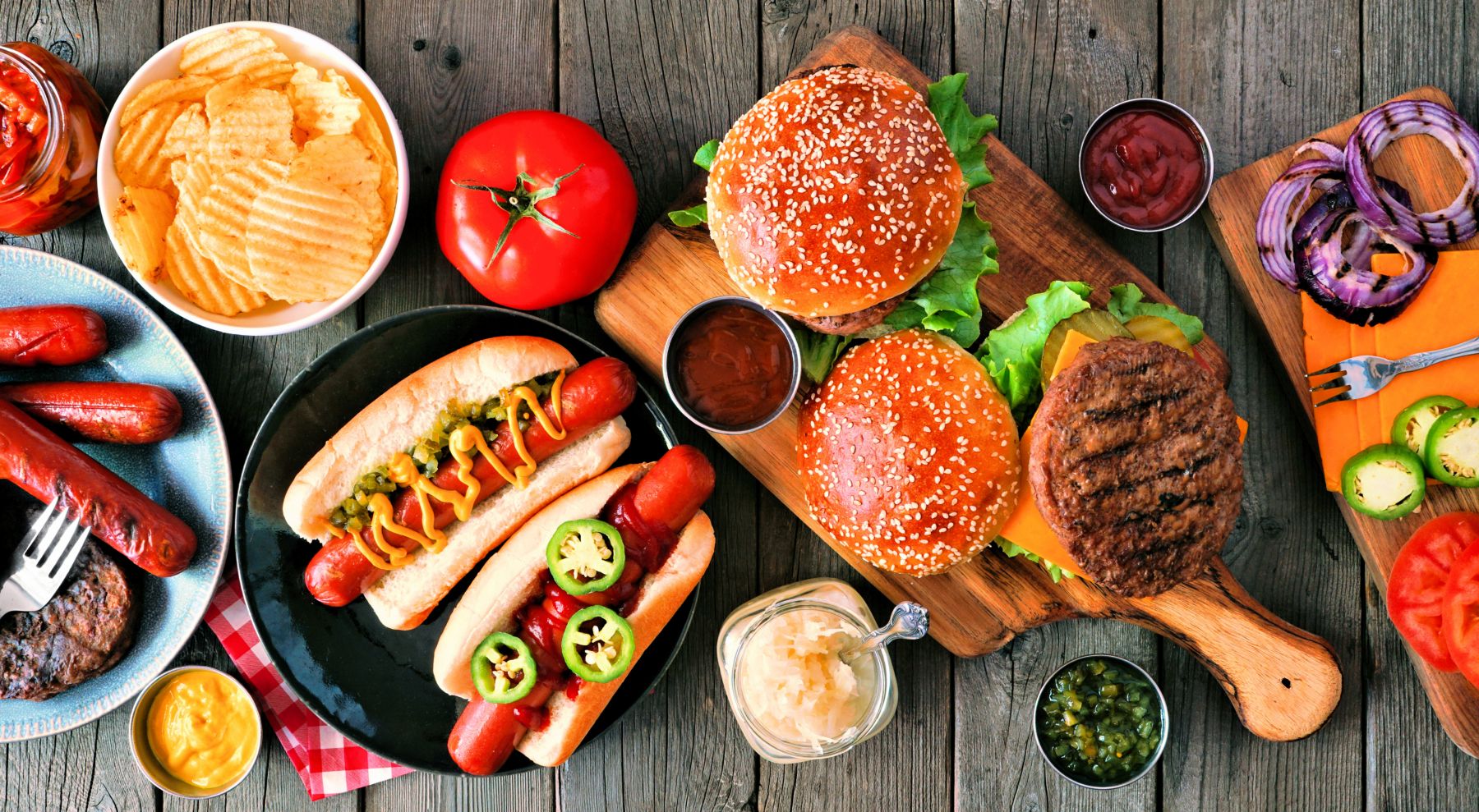 Summer BBQ food table scene with hot dog and hamburger buffet. Above view over a rustic wood background.