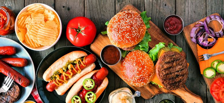 Summer BBQ food table scene with hot dog and hamburger buffet. Above view over a rustic wood background.