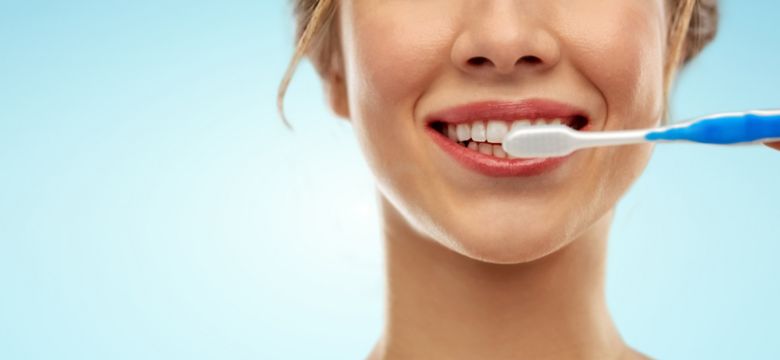 oral care, dental hygiene and people concept - close up of smiling woman with toothbrush cleaning teeth over blue background; Shutterstock ID 1318897805; purchase_order: -; job: -; client: -