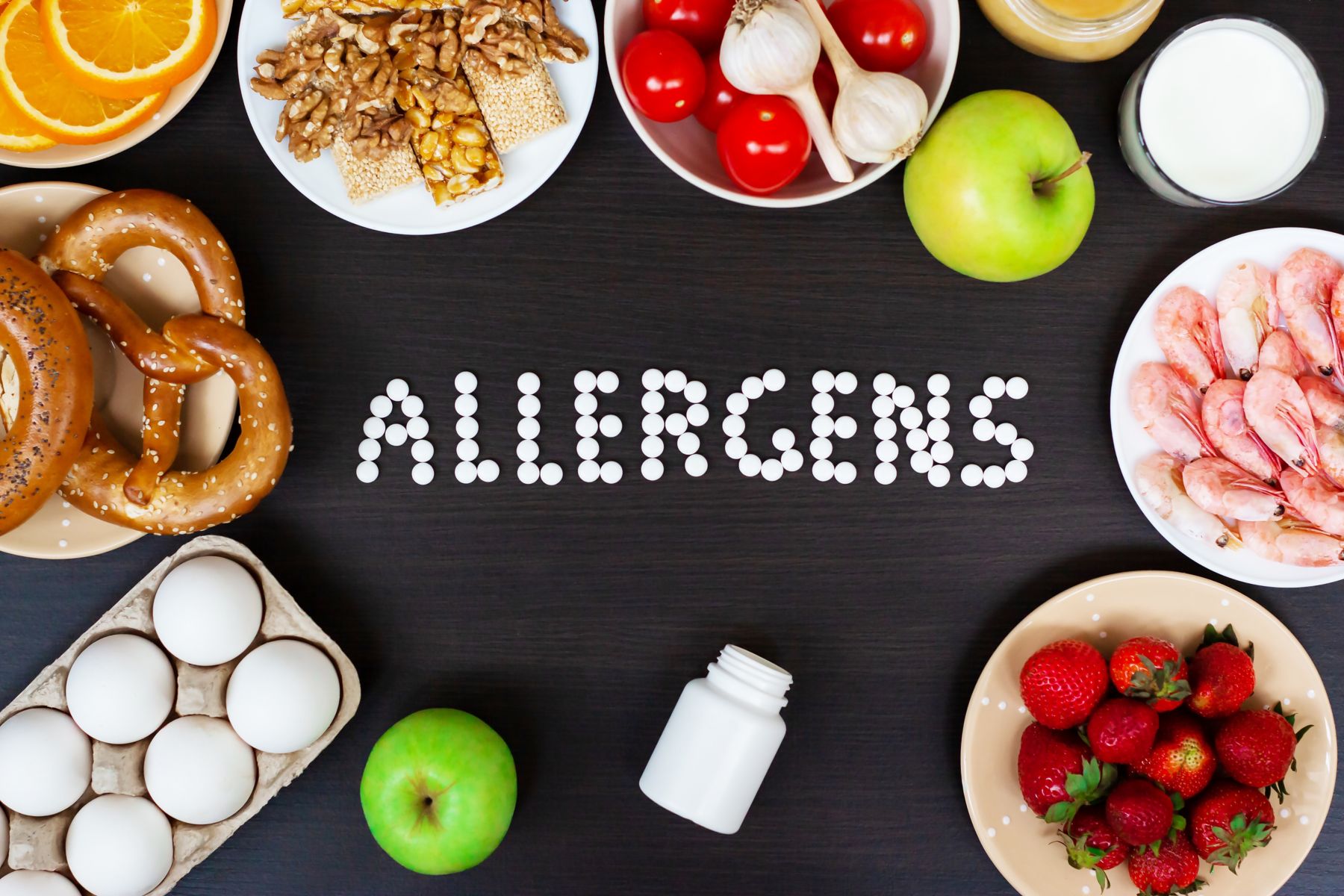 Food allergens as milk, oranges, tomatoes, garlic, shrimp, peanuts, eggs, apples, bread, strawberries on wooden table.; Shutterstock ID 1388739068; BU: KFT; Region: South America; Purpose: Blog post