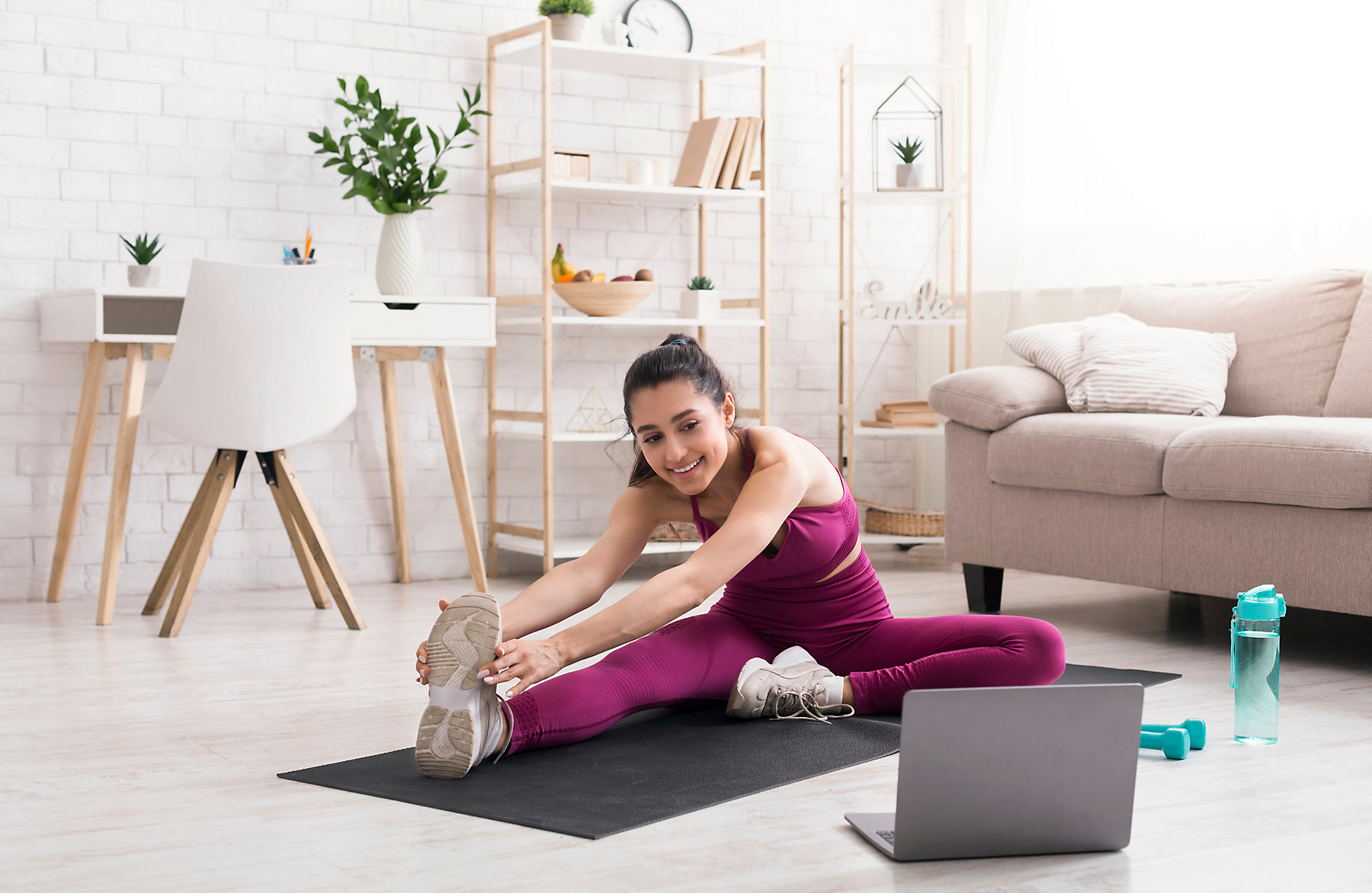 Sports during lockdown. Attractive woman watching online training class and doing stretching exercises at home; Shutterstock ID 1709750248; purchase_order: -; job: -; client: -