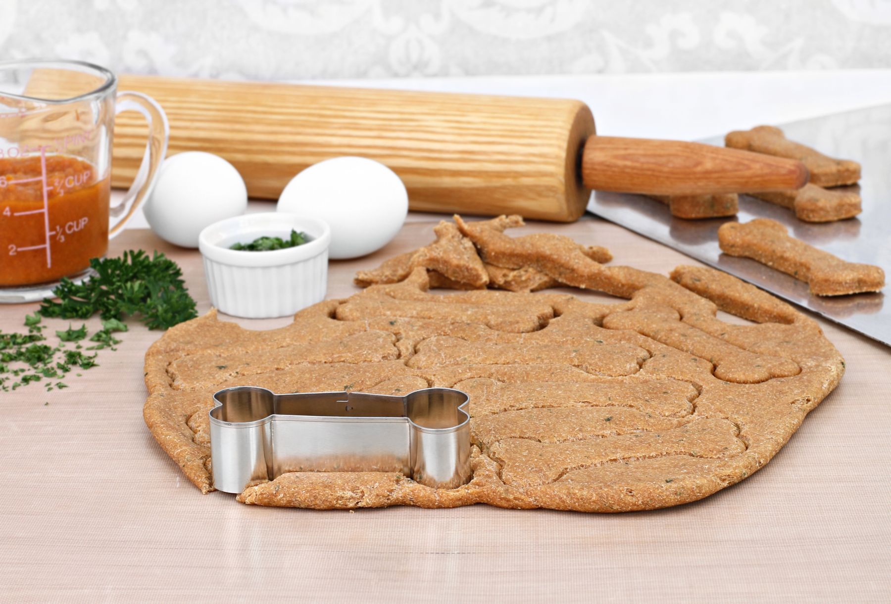 Baking supplies for making homemade healthy pumpkin dog biscuits.  Rolling pin, dough, pumpkin, parsley and eggs next to rolled out dog cookies.  Selective focus on dough.; Shutterstock ID 2024478053; purchase_order: KN; job: EU; client: MARKETING