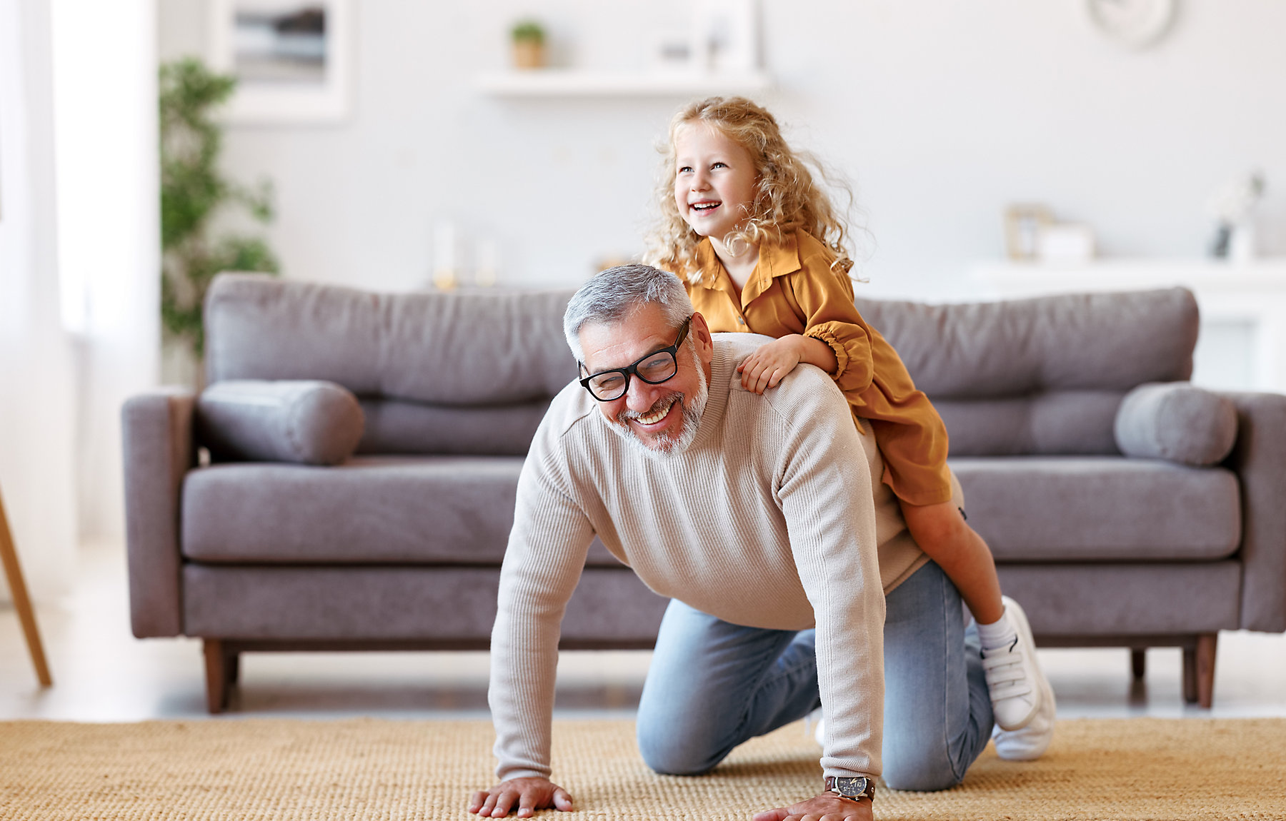 Cute little girl granddaughter playing and having fun with active positive grandfather, senior man grandpa giving piggyback to excited child and smiling at camera while taking care of kid at home; Shutterstock ID 2041162961; purchase_order: -; job: -; client: -