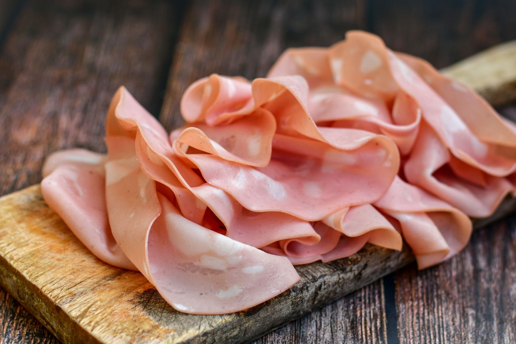 Slices Of  Traditional Italian antipasti mortadella Bolognese  on a wooden  cutting board.