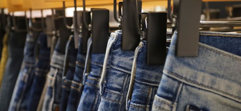 Jeans on the hanger in the store. Clothes on hangers in shop for sale. Blur background. Fashionable clothes in a boutique. Various clothing on market. Shopping in store.