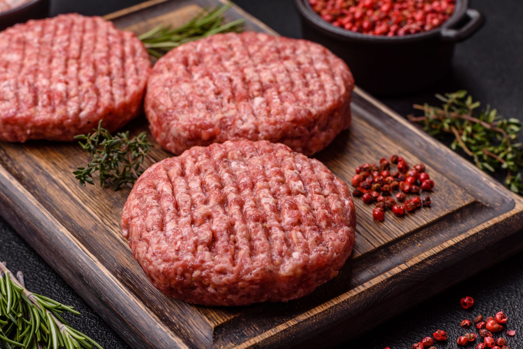 Fresh raw ground beef burger patty with salt and spices on textured concrete background