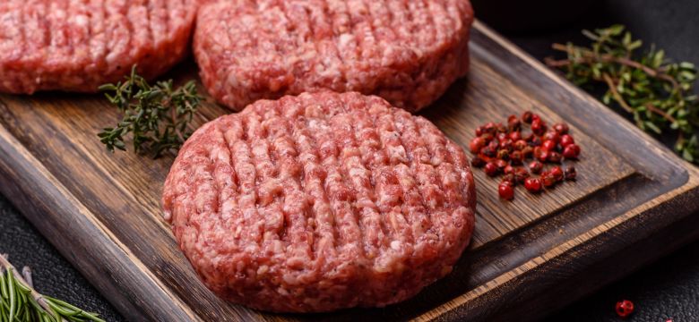 Fresh raw ground beef burger patty with salt and spices on textured concrete background