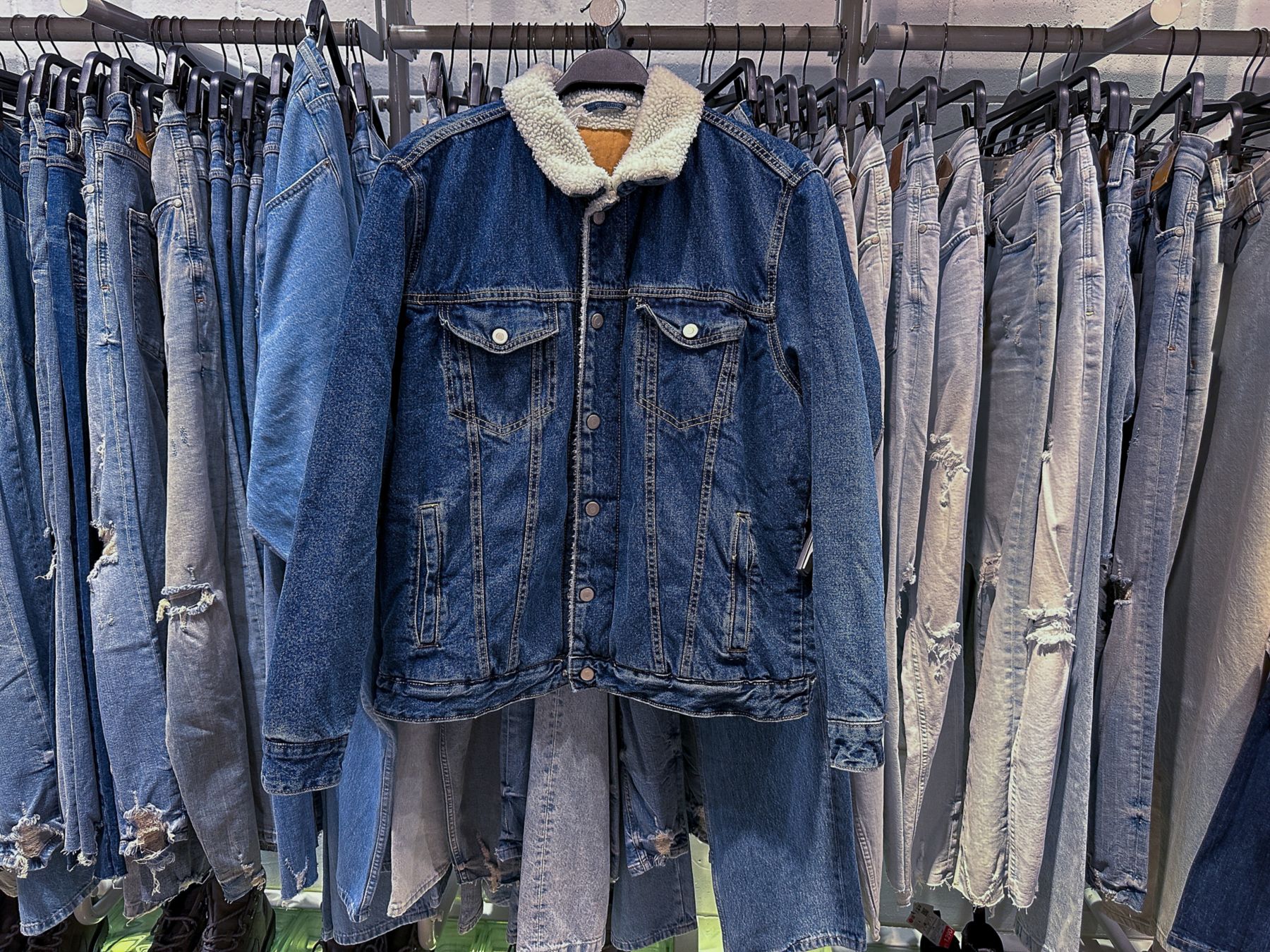 Row of blue jeans with blue jacket on hanger on shop