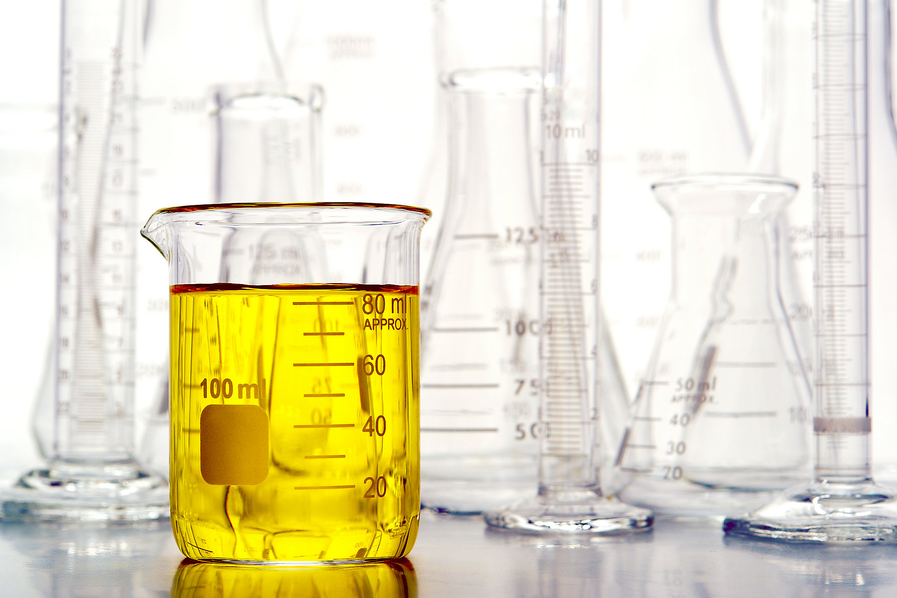 Graduated beaker filled with yellow liquid and laboratory glassware for an experiment in a science research lab
