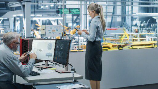 Two colleagues working in manufacturing facility one on a desktop and the other on a phone