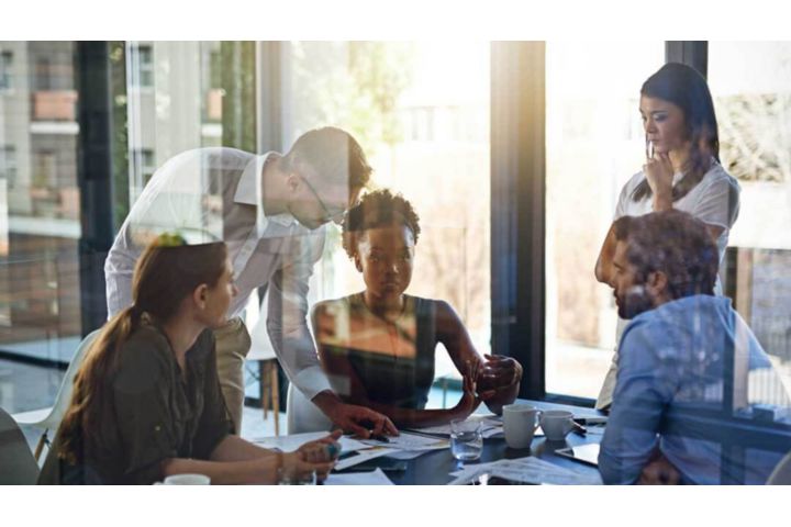 Diverse team collaborating around a table in a modern, sunlit office.