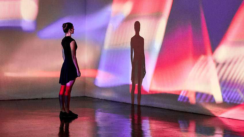 A woman staring at her shadow on a colorful wall.