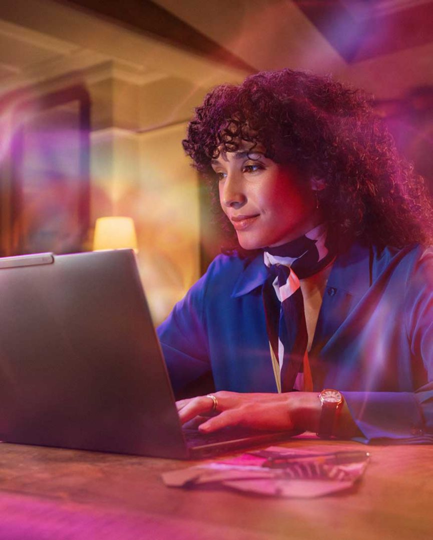 A woman using a laptop with colorful overlays around her.
