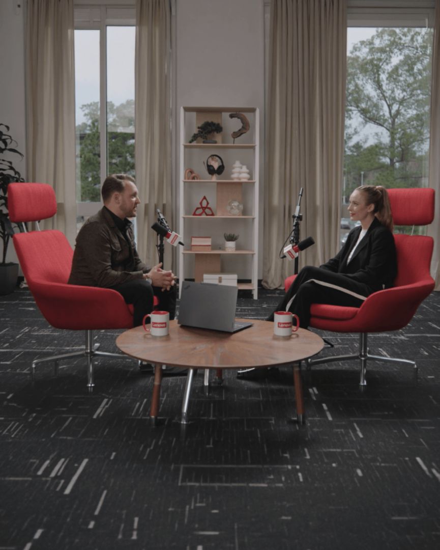 Two people in a Lenovo-branded podcast studio with red chairs.