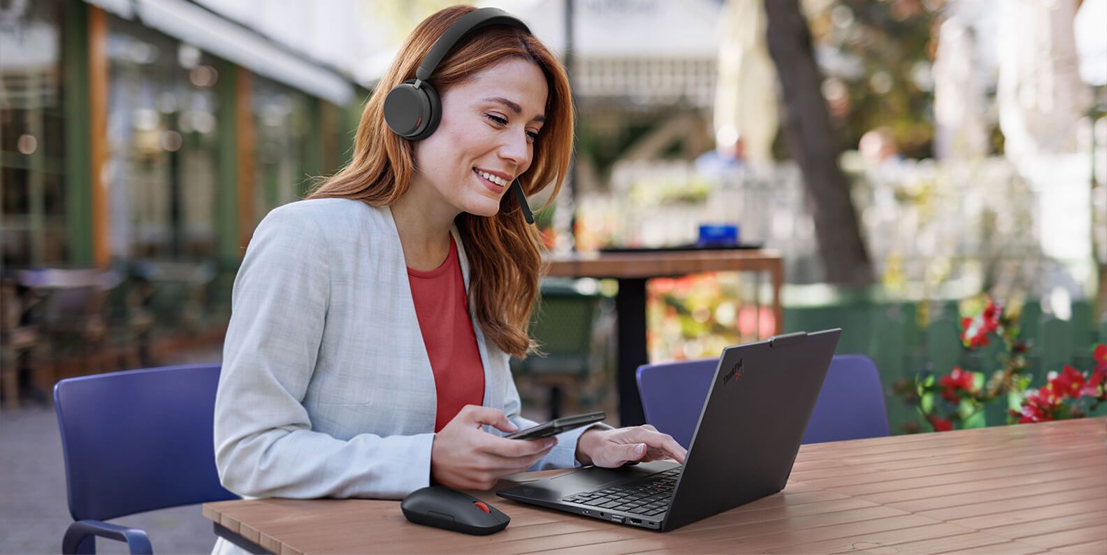 A woman working outside on her laptop and wearing a headset. 