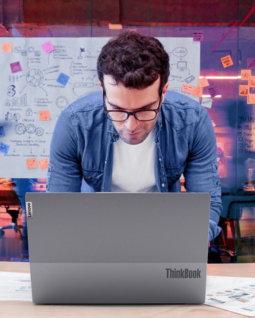 Man working at his Lenovo laptop with post it note board in the background. 