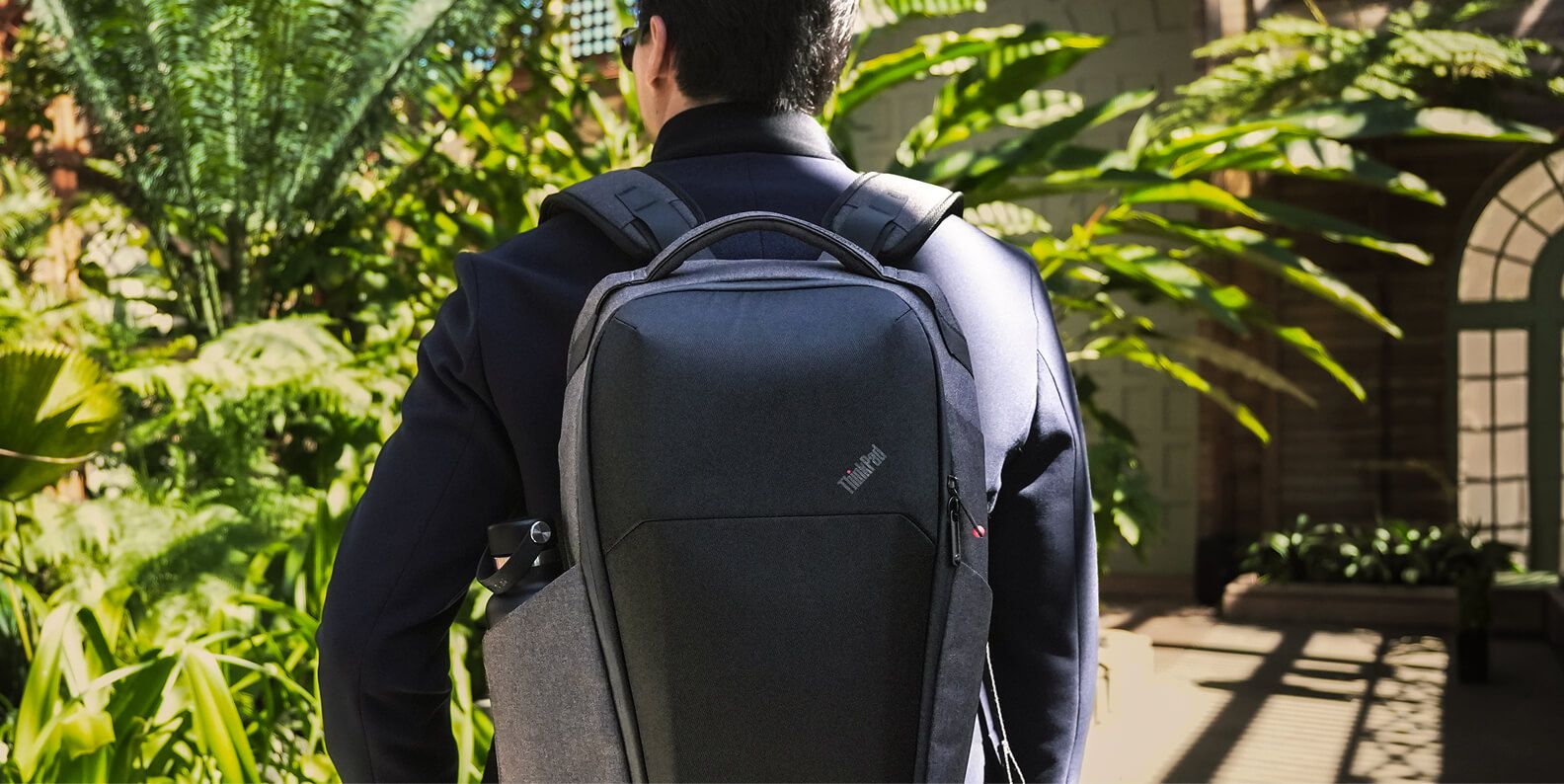 A man walking outside with a black Lenovo backpack.     