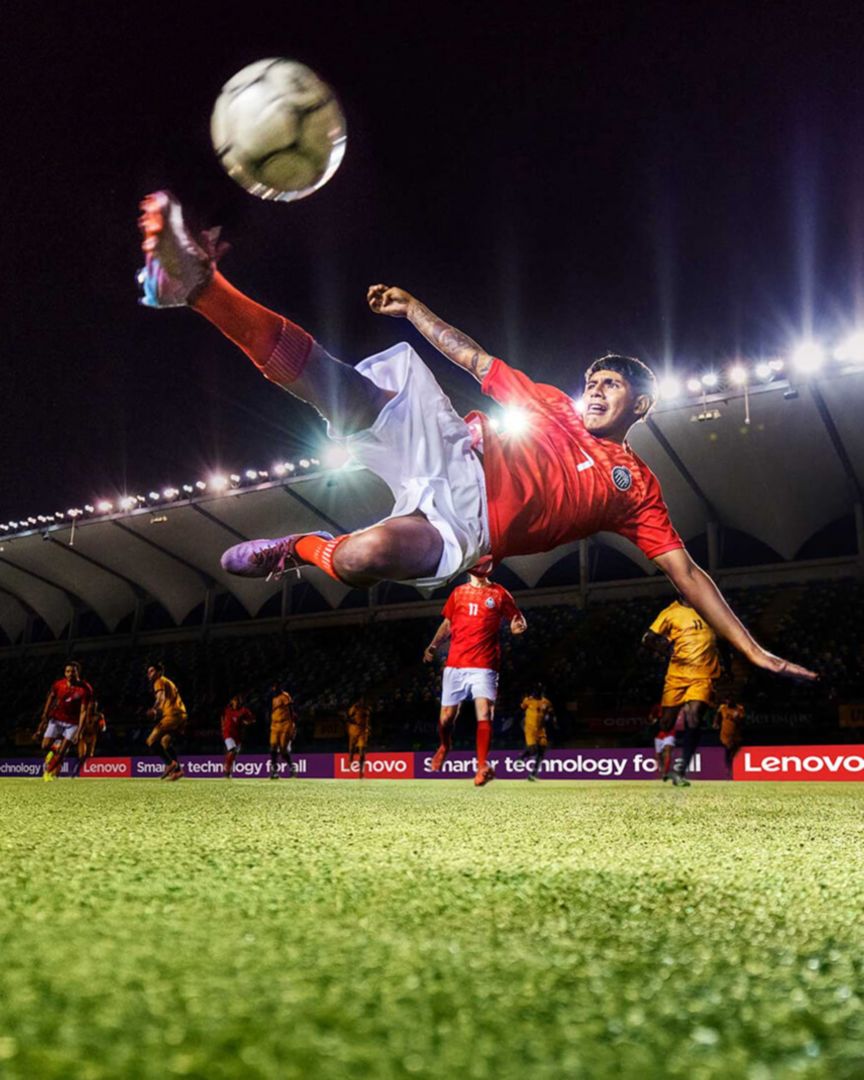 Young man at FIFA performing the bicycle kick soccer move with players in the background.