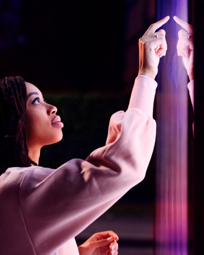 A woman looking at purple and red lights projected on a wall. 