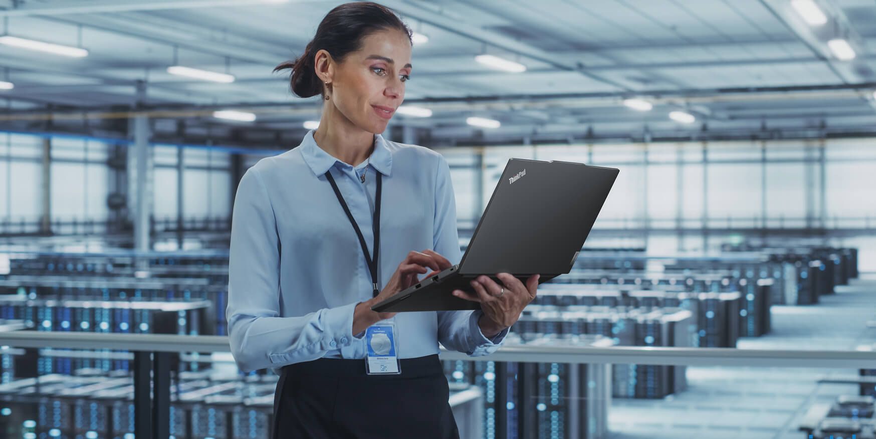 A woman looking at her laptop screen in front of a large room of servers. 