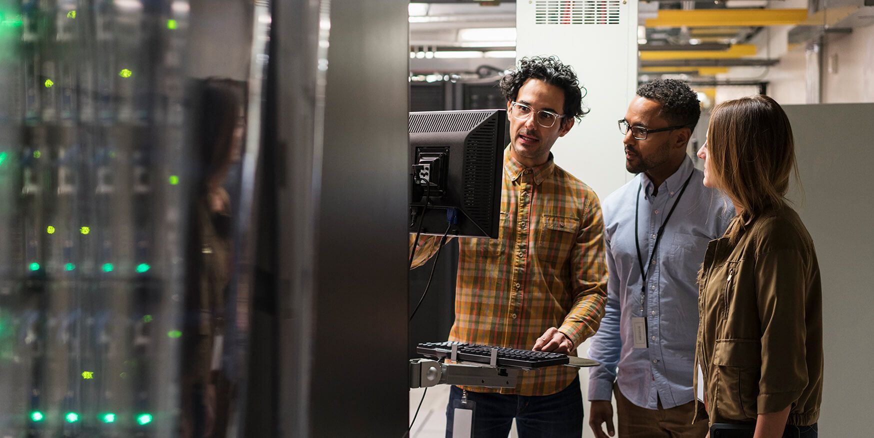 Three colleagues looking at a monitor in a server room. 