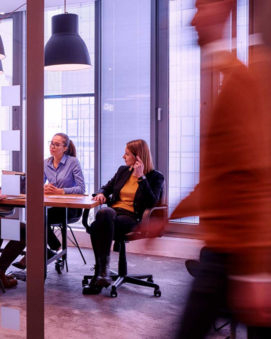 Work colleagues in a glass walled room with a passerby in front.