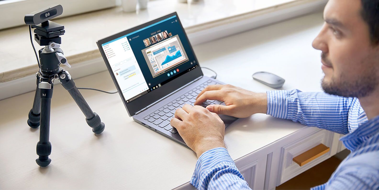 A man using a webcam on an easel and typing on his laptop.  