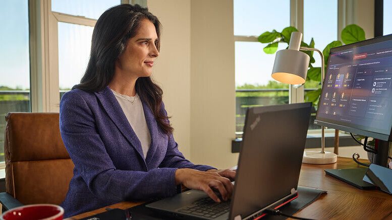 Una mujer escribiendo en su laptop y usando una segunda pantalla en su escritorio en el trabajo.