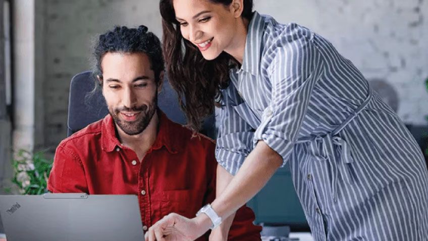 Two colleagues collaborate at a desk with a Lenovo ThinkPad in a modern office.