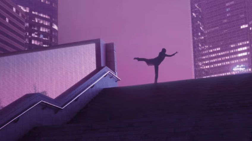 Silhouetted dancer poses on stairs against a purple-lit urban skyline.