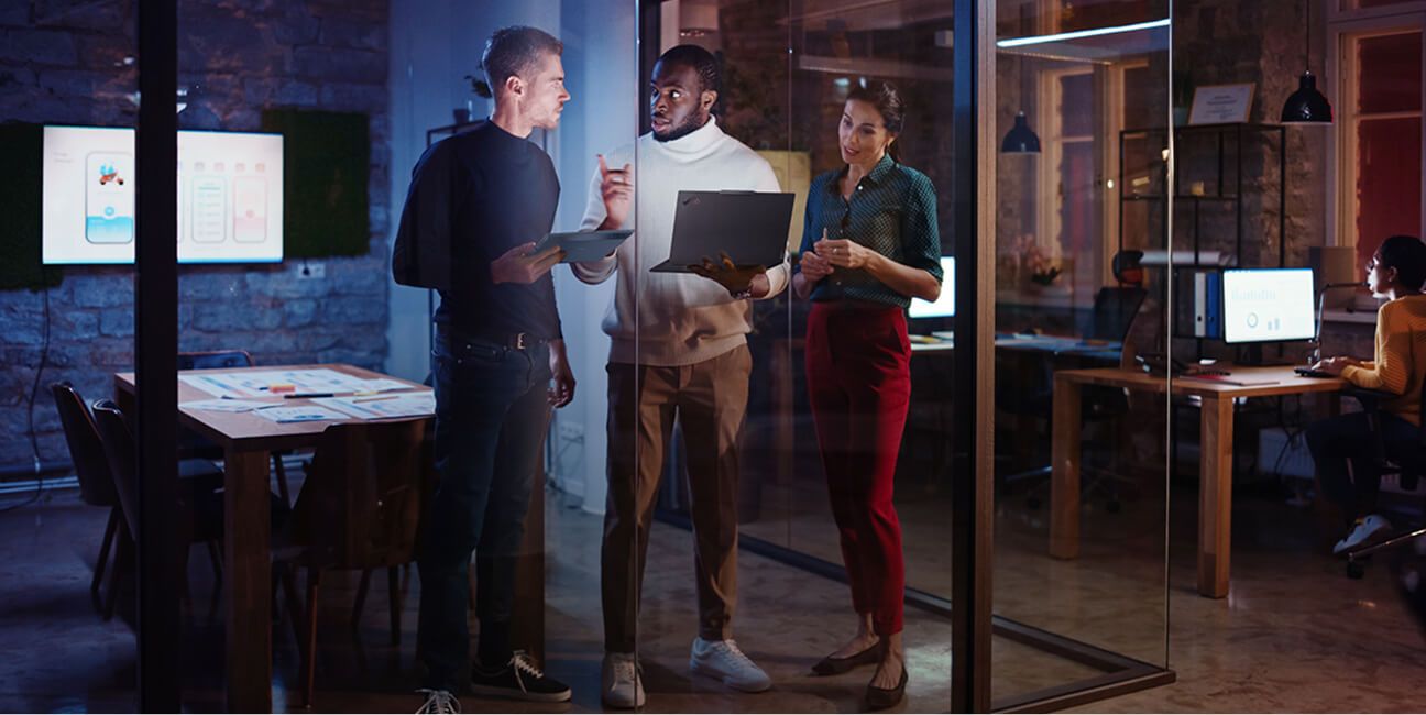 Three colleagues standing and looking at the laptop the middle guy is holding.