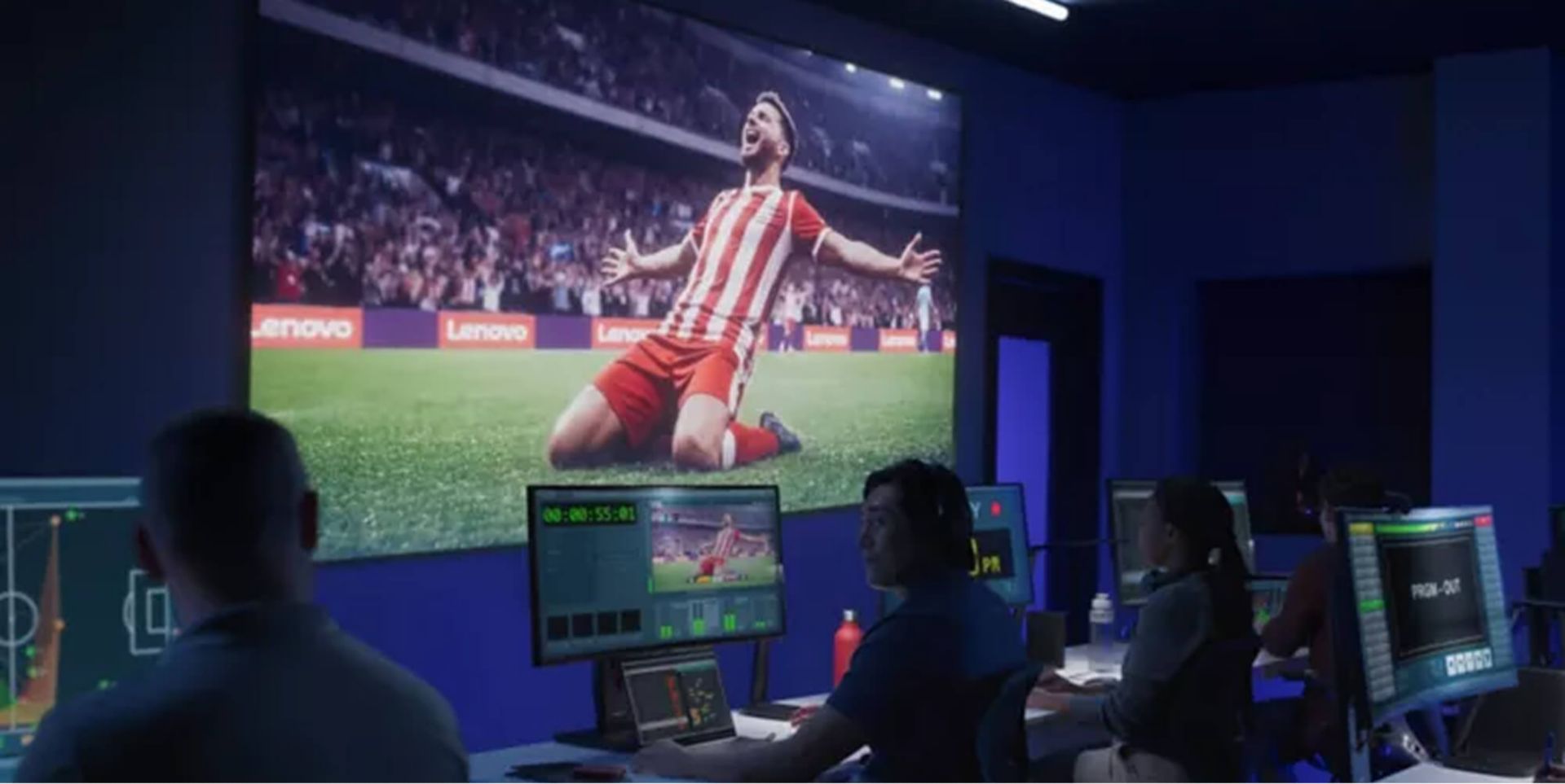 A control room producing a soccer match, with a big screen showing a player sliding on his knees after scoring a goal.
