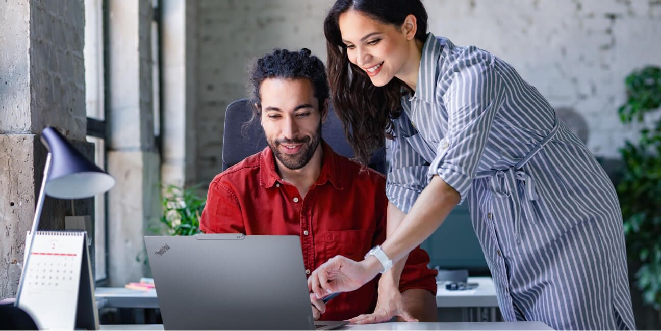 A female colleague pointing over her male colleague's shoulder at his laptop screen. 