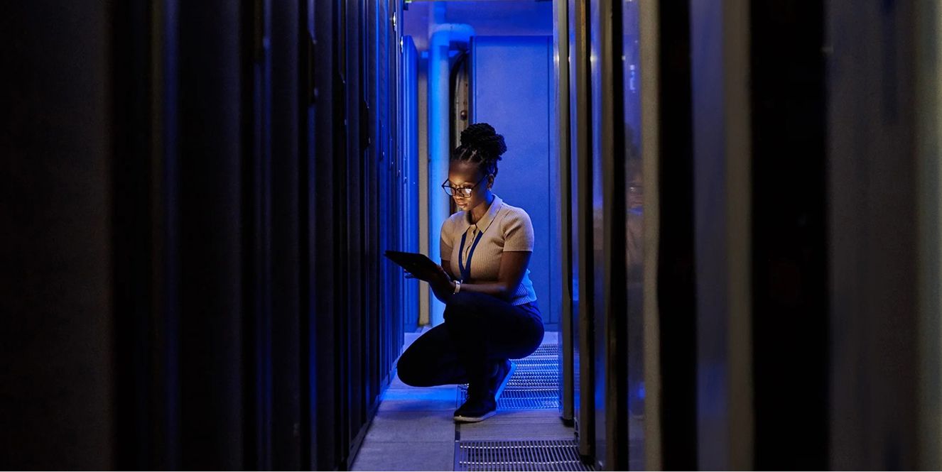 A woman crouching in a server room.