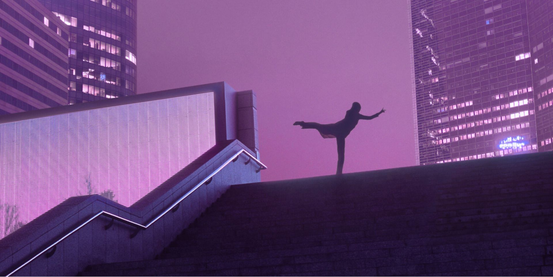A silhouette of a person doing an arabesque at the top of the stairs in front of skyscrapers at night.
