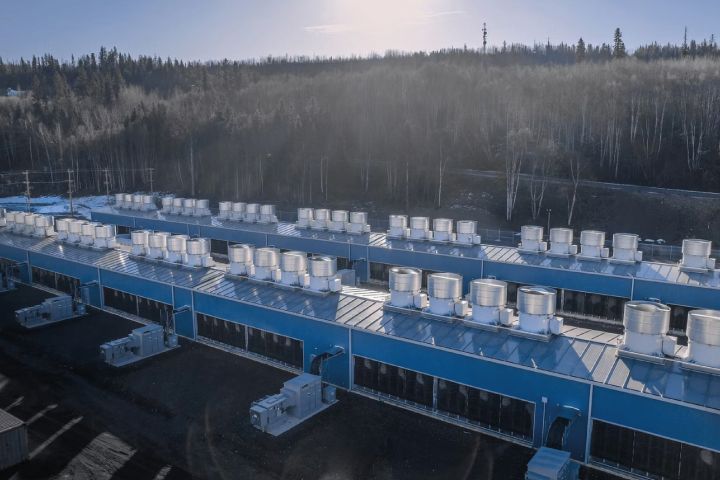 Aerial view of blue industrial buildings in a snowy, forested area.