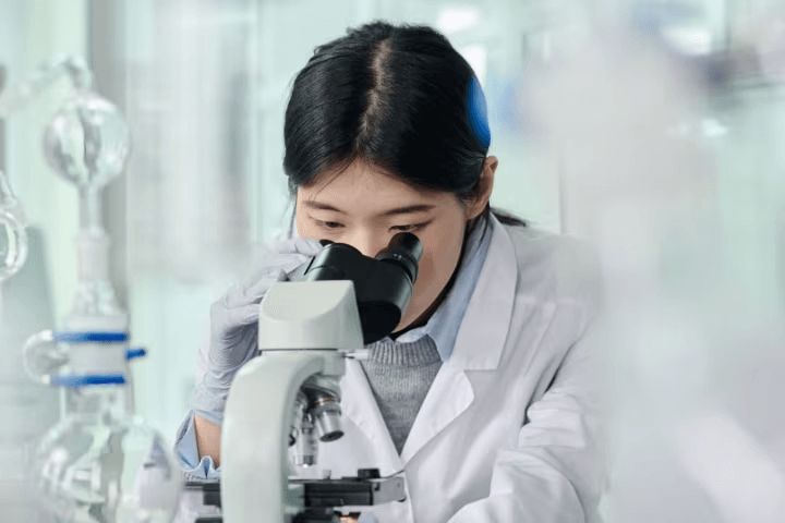 A woman using a microscope in a white labcoat