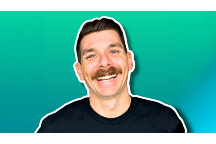 A close-up headshot of a smiling man with a thick, brown mustache. He has dark hair styled neatly to the side and is wearing a plain black t-shirt. The man’s image is outlined with a thin white border and set against a solid teal-green background with a subtle drop shadow.