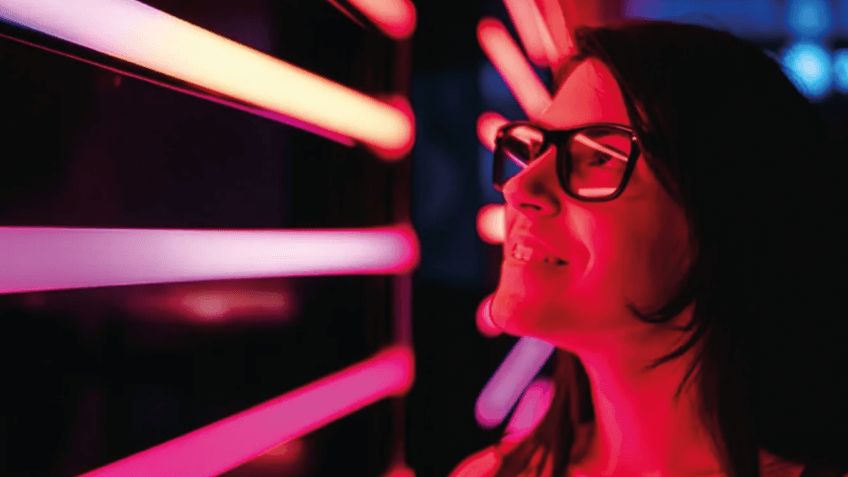 A woman wearing glasses looking into red tubes of light