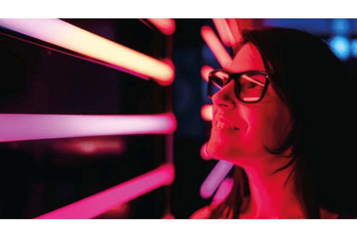 A woman wearing glasses looking into red tubes of light