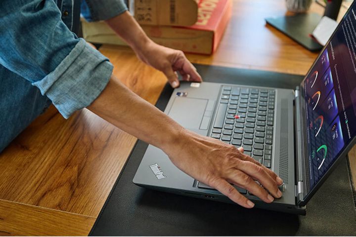 Hands setting an open laptop on a desk.
