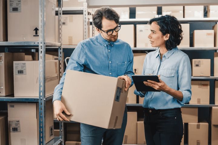 A man holding a box speaking to a women holding a tablet