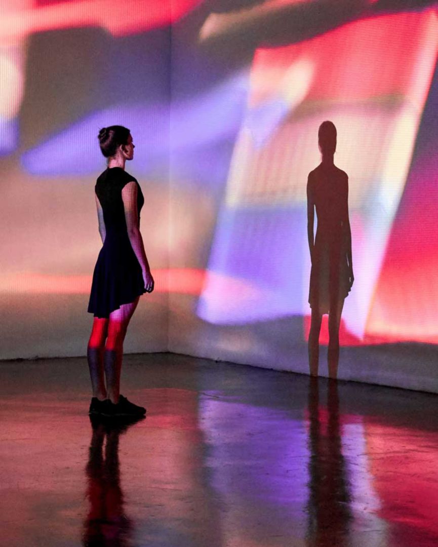 A woman looking at purple and red lights projected on a wall. 