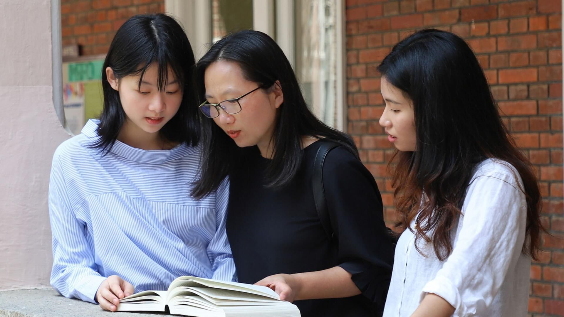 Three students looking at the same book. 