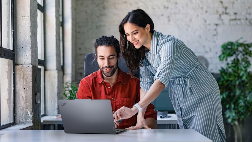 Two colleagues collaborate at a desk with a Lenovo ThinkPad in a modern office.