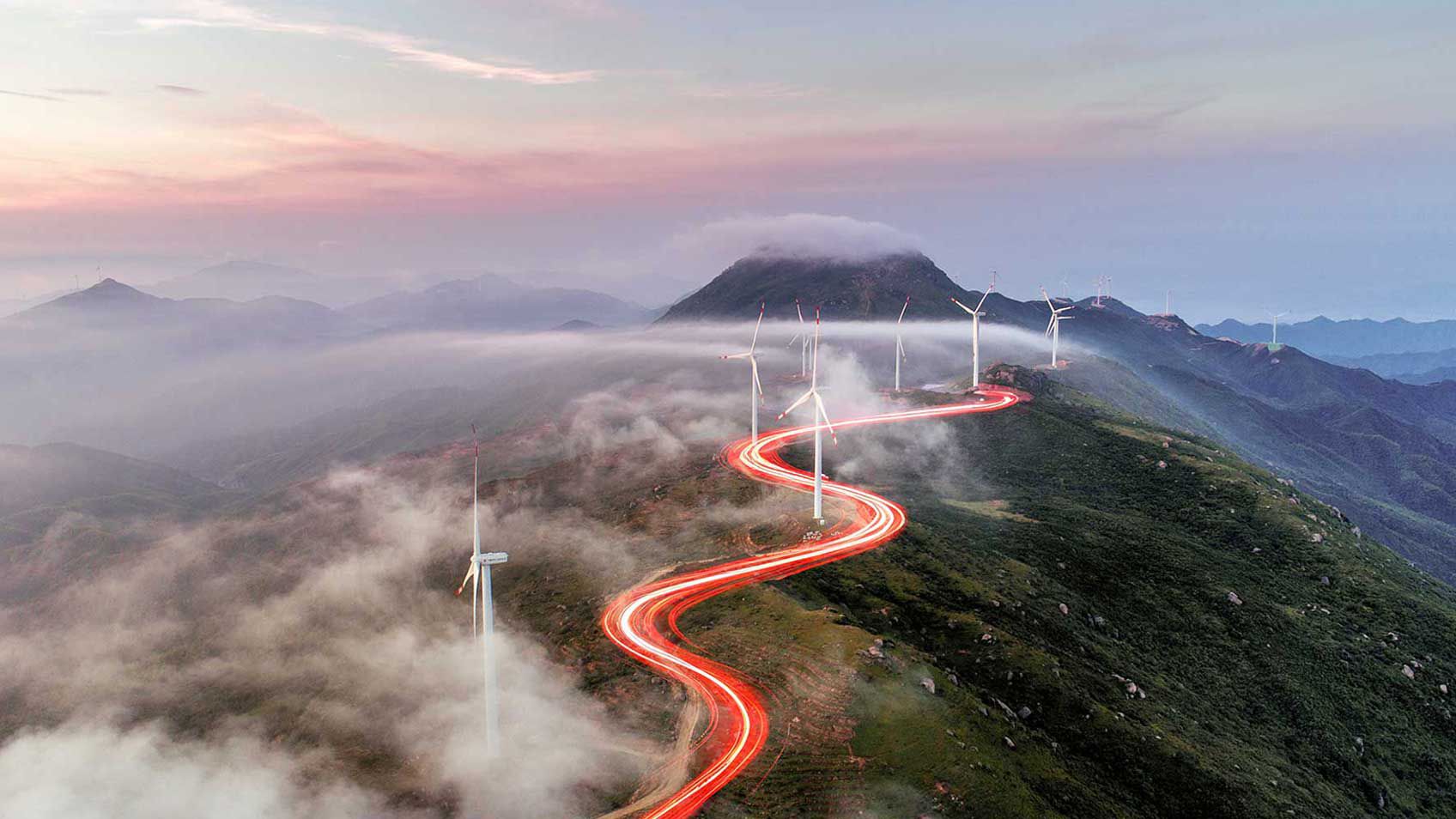 A red light weaving through wind turbines on hill tops.