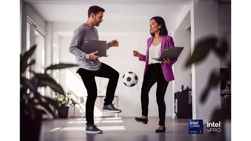 Two colleagues standing in a hallway and kicking a soccer ball back and forth.